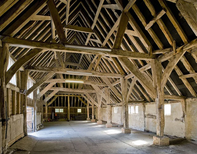 Interior of an empty barn, with exposed timber posts and roof trusses above a broad floor.