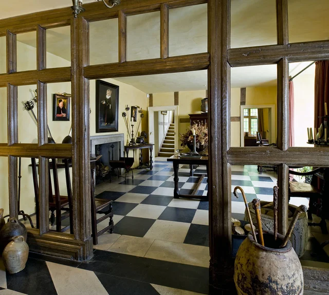 A view through an exposed timber screen into a hallway with a black-and-white chequered floor.