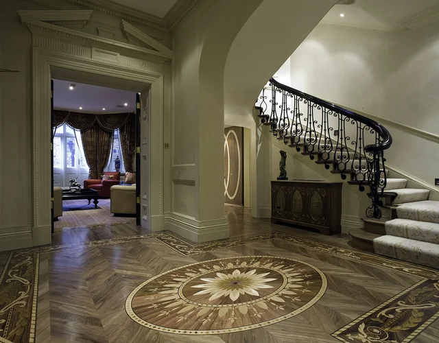A pale entrance hall with a curved staircase, decorative dark balustrade and a circular star motif set into the floor.
