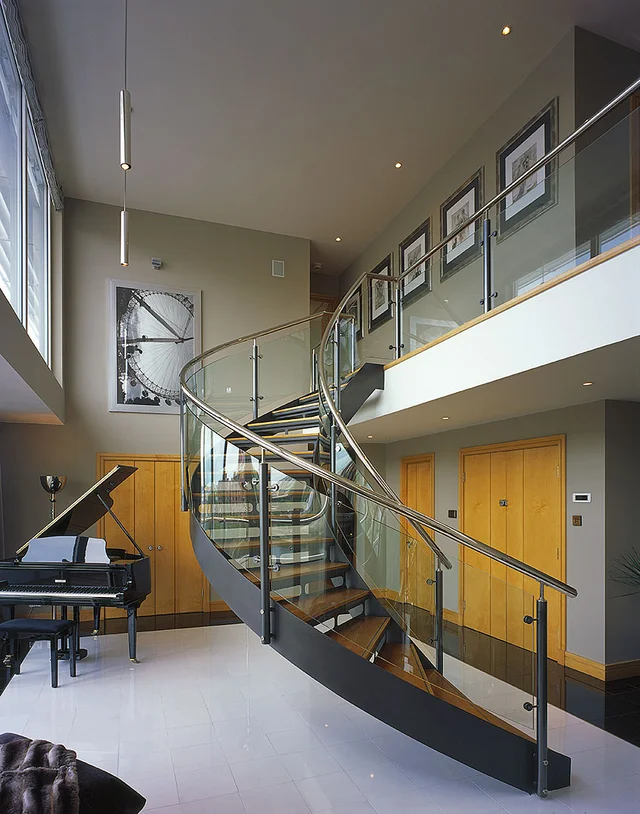 A modern open hall with a curving metal staircase, a high window and a gallery of framed pictures.