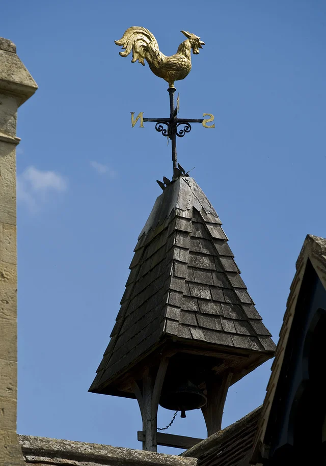 A golden cockerel weather vane stands above a small pointed roof against a clear blue sky.