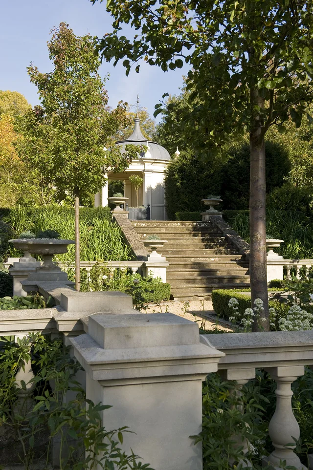 Stone balustrades and planted terraces frame a flight of garden steps leading towards a pale pavilion.