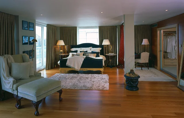 A spacious bedroom with slender columns, a chaise longue and a bed beneath a curved headboard.