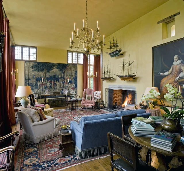 A high-ceilinged drawing room with a lit fireplace, chandelier, patterned rugs and clustered seating.