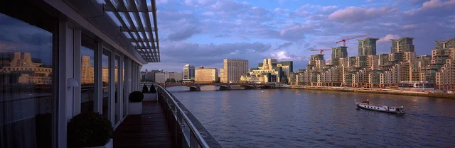 A covered balcony overlooks a river, boats and a skyline of closely spaced buildings.