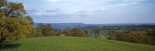 A sloping lawn and autumn-coloured trees overlook distant fields and a broad horizon.