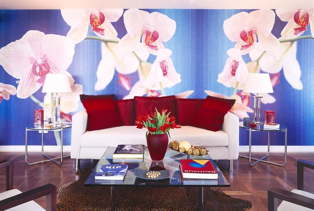 A white sofa with red cushions sits beneath an oversized orchid image on a blue wall.