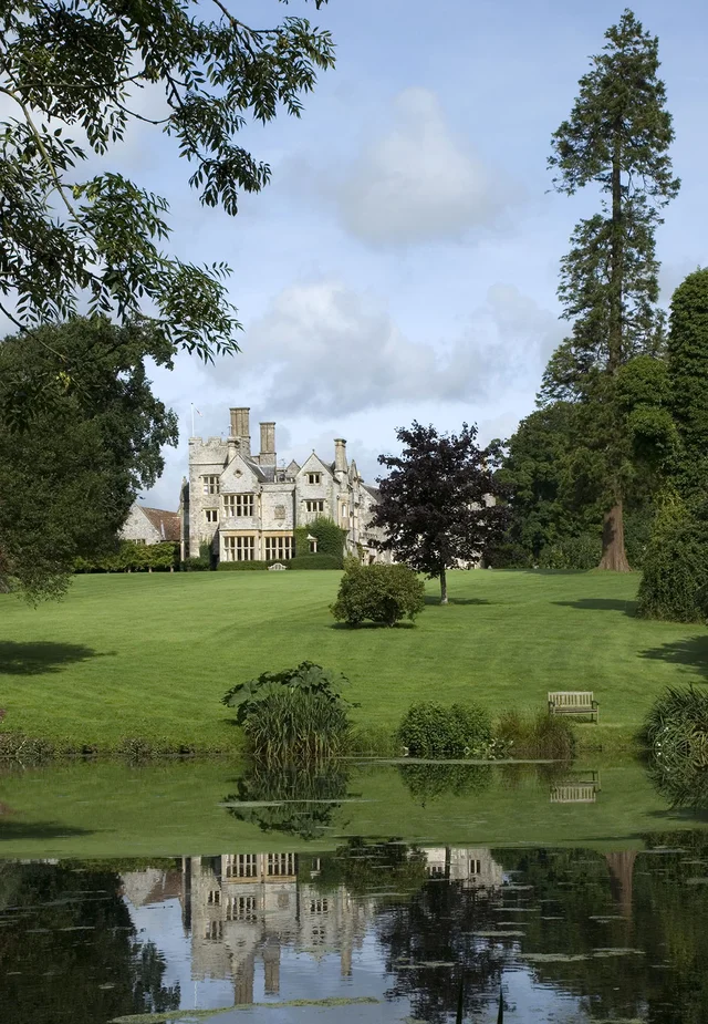 A distant house stands beyond an expansive lawn, framed by trees and reflected in a foreground pond.