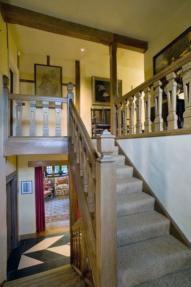 A straight staircase rises to an open gallery with balustrades and warm yellow walls.