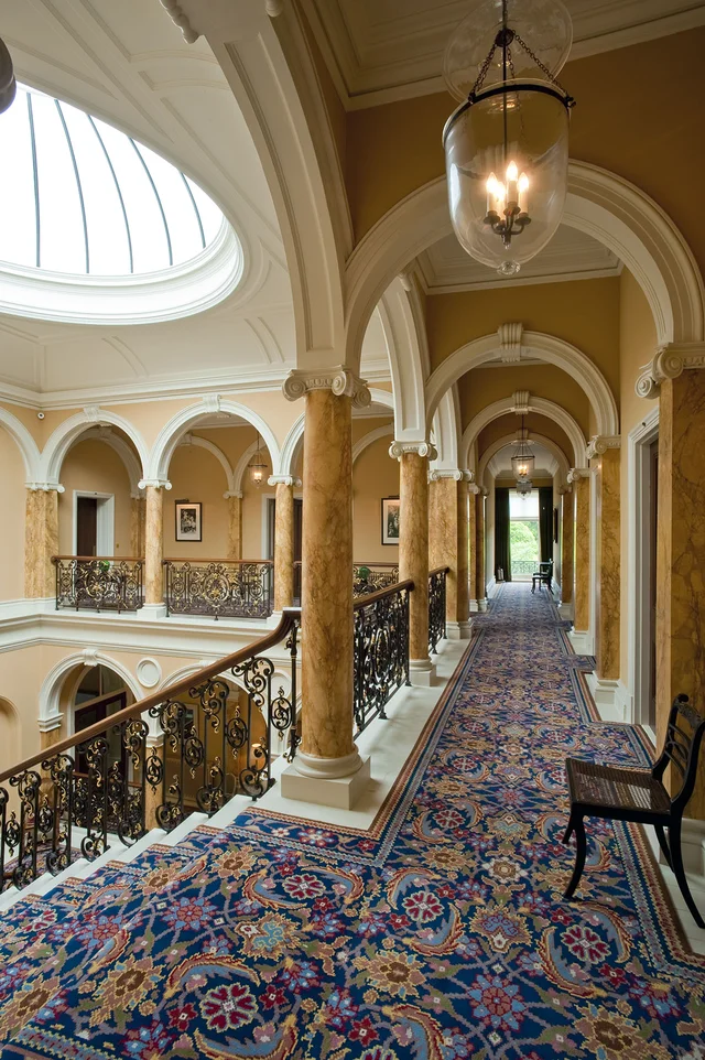 An upper gallery with patterned blue carpet runs beneath arches beside an ornate balustrade.