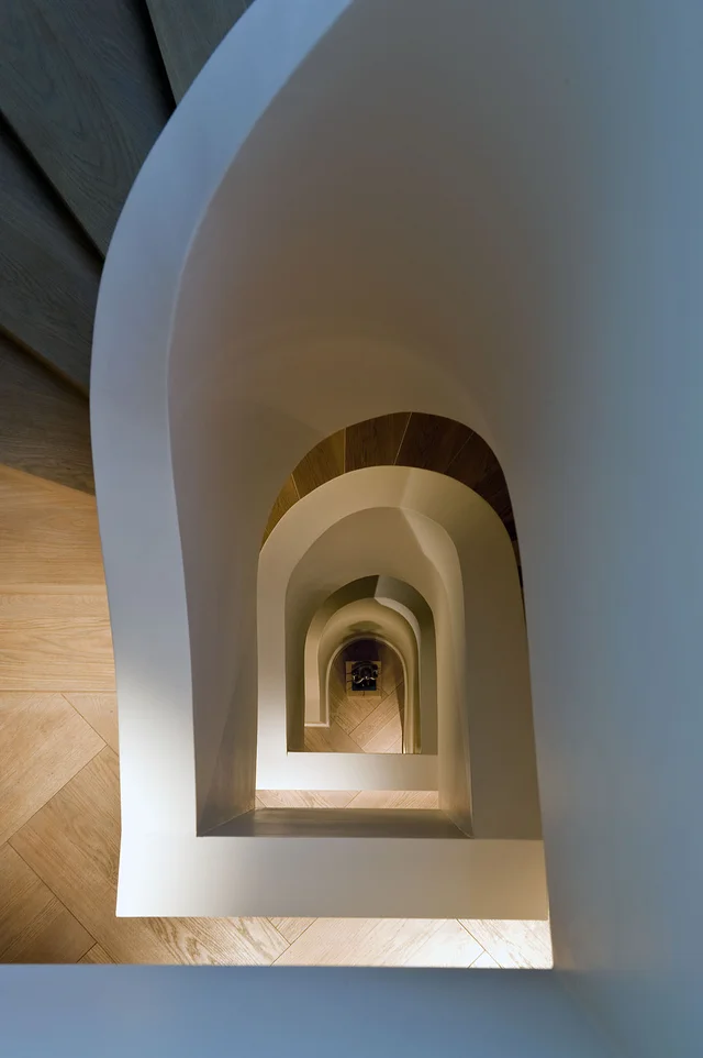 A view down a smooth-walled stairwell shows repeating curved openings receding through successive floors.